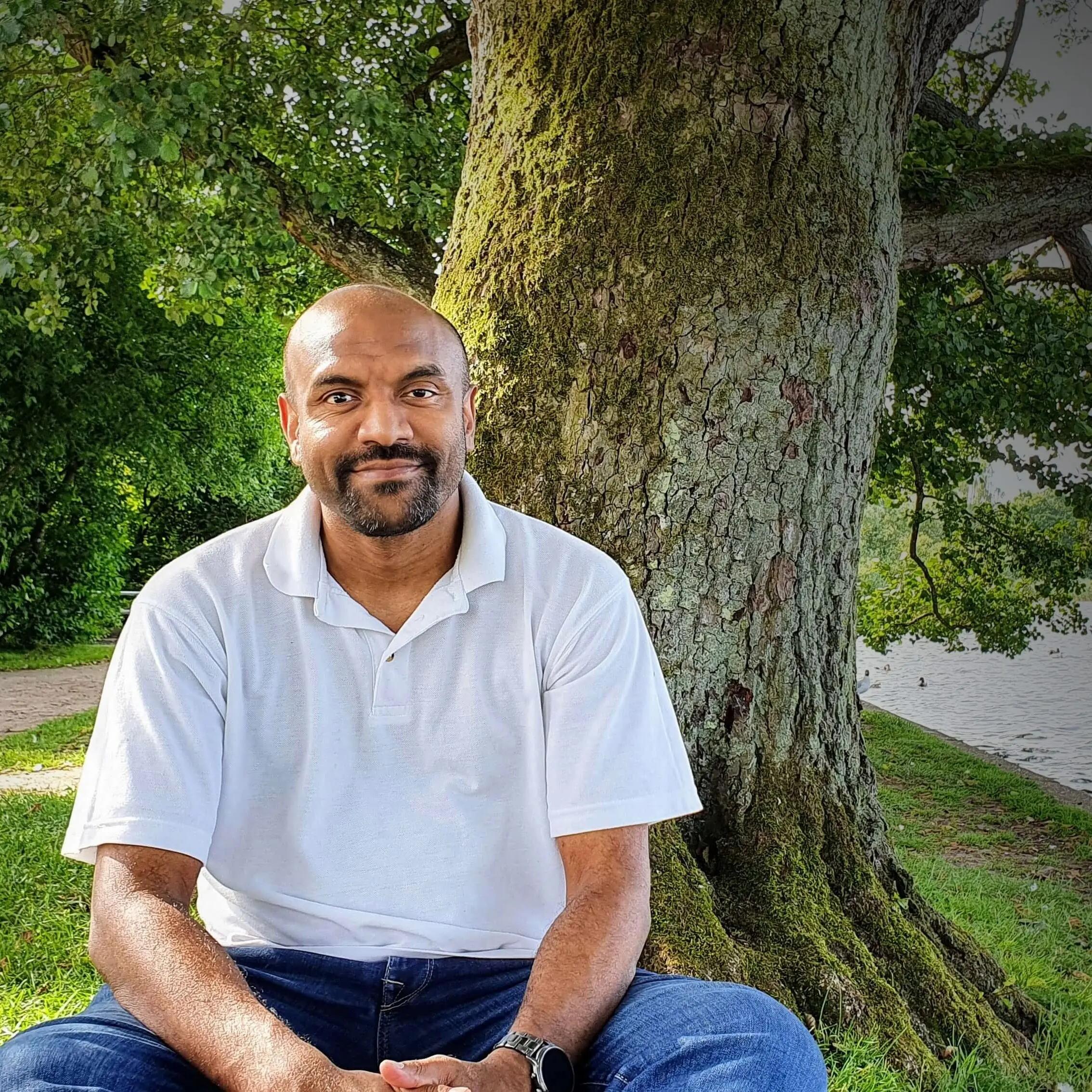 Kumaran Kumarathurai sitting under a large tree by a lake in Aarhus